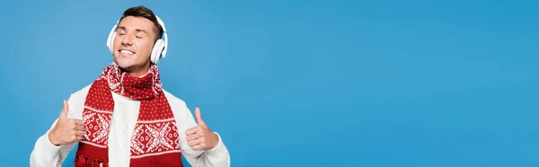 Щасливий чоловік із закритими очима, показує великі пальці вгору, вдягнені в бездротові навушники ізольовані на синьому, банер — Stock Photo