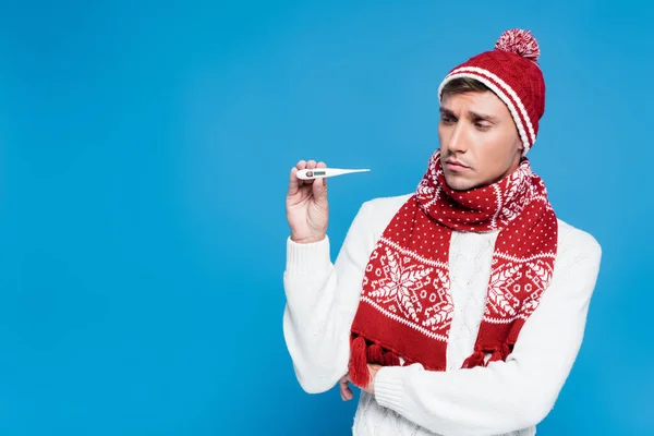 Sick and upset man in knitwear showing  thermometer isolated on blue — Stock Photo