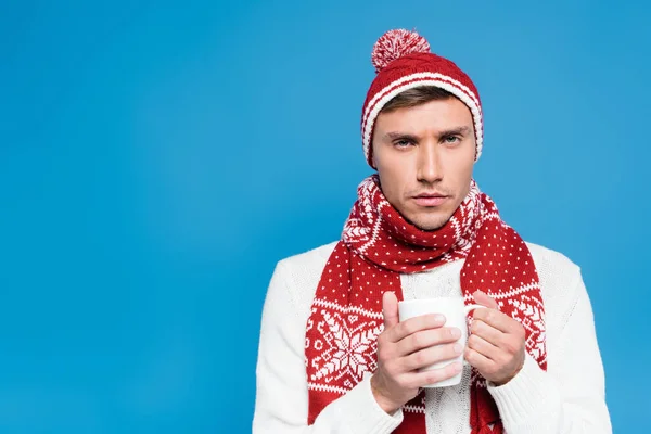 Sick young adult man in knitwear holding cup and looking at camera isolated on blue — Stock Photo