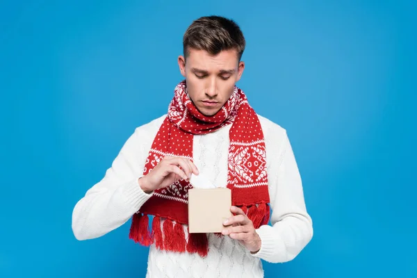 Inquiète jeune homme adulte en écharpe rouge tenant boîte de tissus isolés sur bleu — Photo de stock