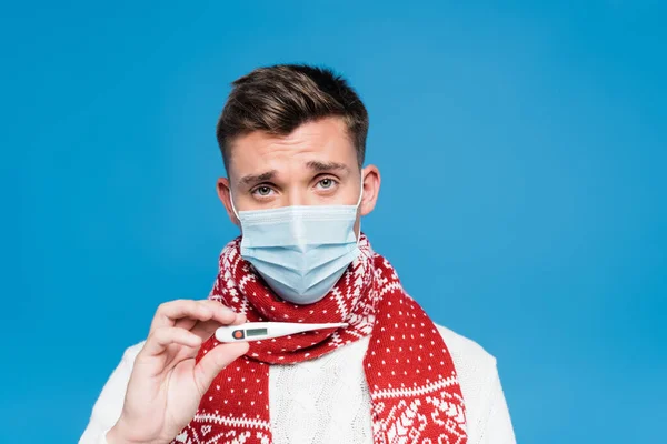 Retrato de homem em máscara médica mostrando termômetro isolado em azul — Fotografia de Stock