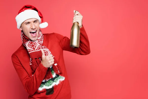 Eccitato uomo in cappello di Babbo Natale mostrando come gesto e tenendo in mano bottiglia di champagne su sfondo rosso — Foto stock