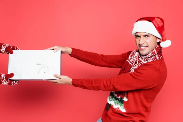 Smiling man in santa hat pulling present on red background — Stock Photo