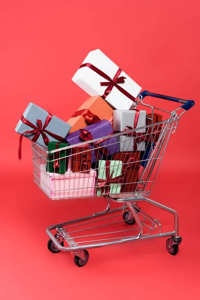 Gift boxes with bows in shopping cart on red background — Stock Photo