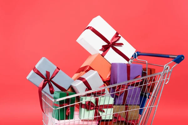 Presentes coloridos com arcos no carrinho de compras no fundo vermelho — Fotografia de Stock