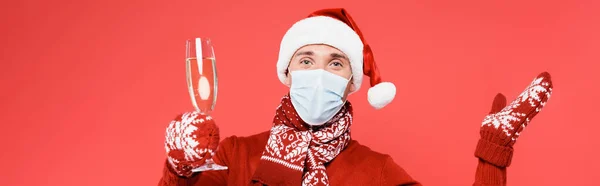 Chapeau homme au Père Noël et masque médical tenant un verre de champagne isolé sur rouge, bannière — Photo de stock