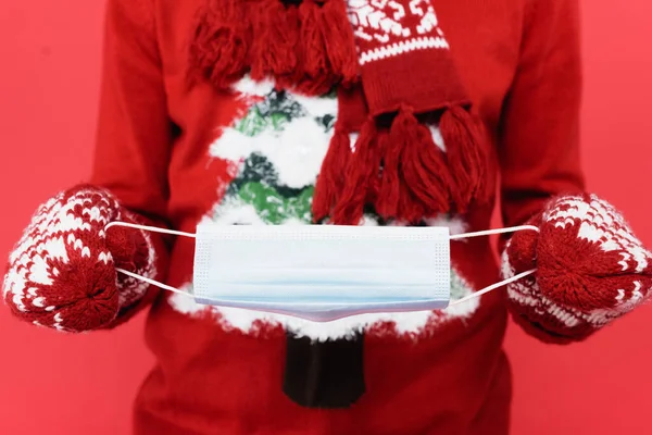 Cropped view of man in mittens holding medical mask on blurred background isolated on red — Stock Photo