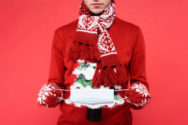 Cropped view of man in scarf and mittens holding medical mask isolated on red — Stock Photo