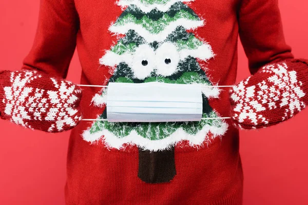 Cropped view of man in mittens and sweater holding medical mask isolated on red — Stock Photo