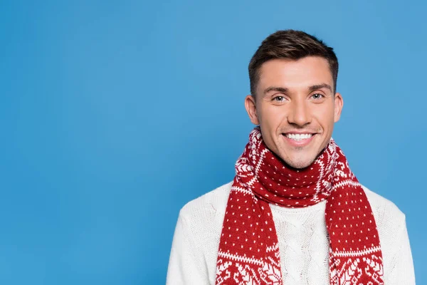 Hombre joven en suéter y bufanda sonriendo a la cámara aislado en azul - foto de stock