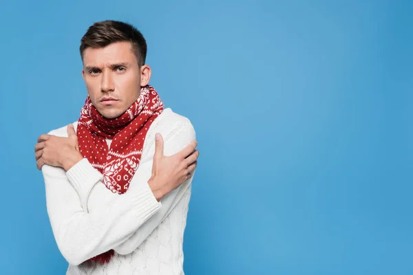 Young man in sweater and scarf feeling cold isolated on blue — Stock Photo