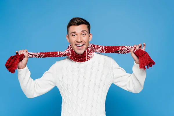 Cheerful man in sweater holding scarf and looking at camera on blue background — Stock Photo