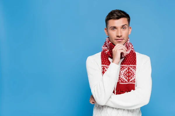 Young man in scarf with hand near chin looking at camera on blue background — Stock Photo