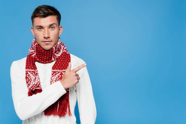 Young man in sweater and scarf pointing with finger isolated on blue — Stock Photo