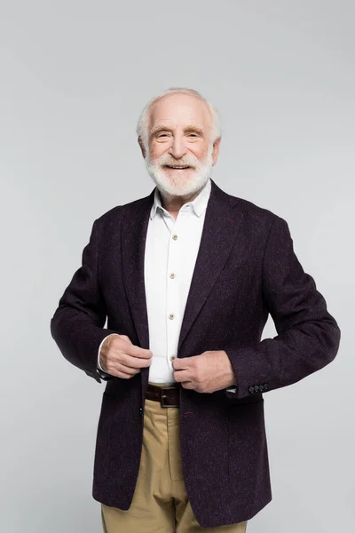 Smiling senior man looking at camera while touching jacket isolated on grey — Stock Photo