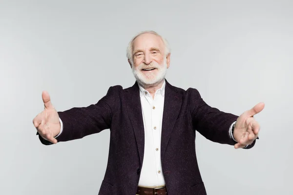 Homme âgé souriant en chemise et veste tirant la main à la caméra sur l'avant-plan flou isolé sur gris — Photo de stock