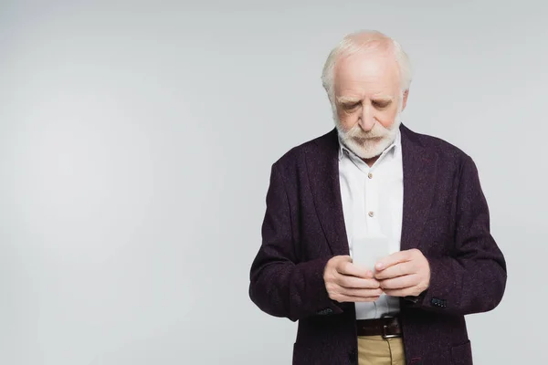 Elderly man in shirt and jacket using smartphone isolated on grey — Stock Photo