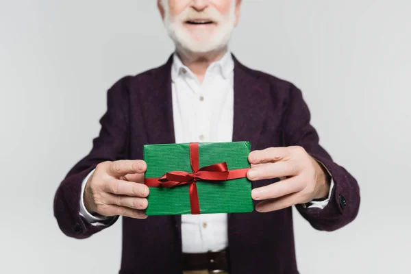 Обрезанный вид подарочной коробки в руках улыбающегося пожилого человека на размытом фоне, изолированном на сером — стоковое фото