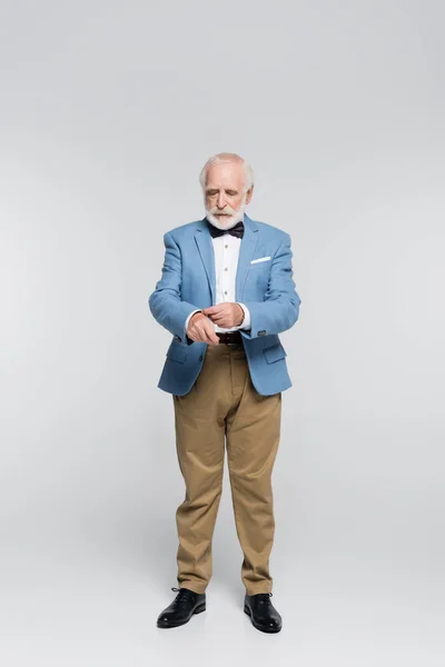 Senior man in bow tie touching jacket on grey background — Stock Photo