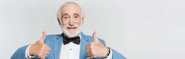 Hombre mayor sonriente con pajarita mostrando los pulgares hacia arriba aislado en gris, estandarte - foto de stock