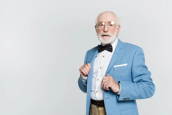 Homme âgé en veste et noeud papillon regardant la caméra isolée sur gris — Photo de stock