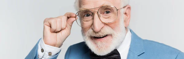 Vieil homme souriant touchant des lunettes isolées sur gris, bannière — Photo de stock