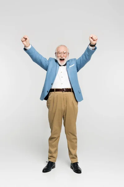 Excited senior man in blue jacket and eyeglasses showing yes gesture on grey background — Stock Photo