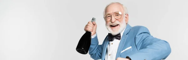 Homme âgé souriant en noeud papillon tenant une bouteille de champagne isolée sur fond gris, bannière — Photo de stock