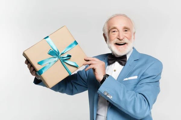Homme âgé souriant en noeud papillon et veste tenant cadeau isolé sur gris — Photo de stock