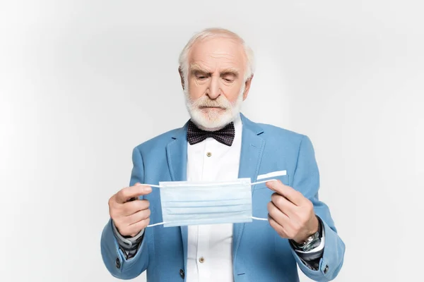 Senior man in jacket and bow tie holding medical mask isolated on grey — Stock Photo