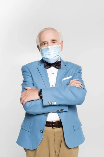 Hombre de pelo gris con máscara médica con brazos cruzados mirando a la cámara aislada en gris - foto de stock