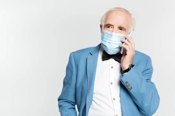 Hombre mayor en máscara médica hablando en el teléfono inteligente aislado en gris - foto de stock
