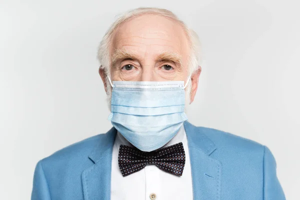 Senior man in medical mask and jacket with bow tie looking at camera isolated on grey — Stock Photo