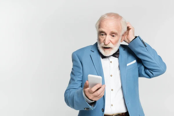 Emocionado hombre mayor en corbata de lazo y chaqueta sosteniendo teléfono inteligente aislado en gris - foto de stock