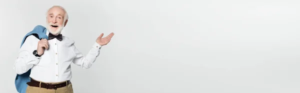 Smiling senior man pointing with hand while holding jacket isolated on grey, banner — Stock Photo