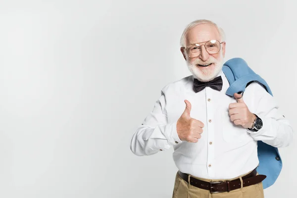 Homem sênior sorrindo para a câmera enquanto mostra o polegar para cima gesto e segurando casaco azul isolado no cinza — Fotografia de Stock