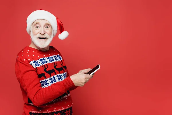 Lächelnder älterer Mann mit Weihnachtsmütze und rotem Smartphone — Stockfoto