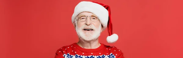 Allegro uomo anziano in occhiali e cappello di Babbo Natale isolato su rosso, striscione — Foto stock