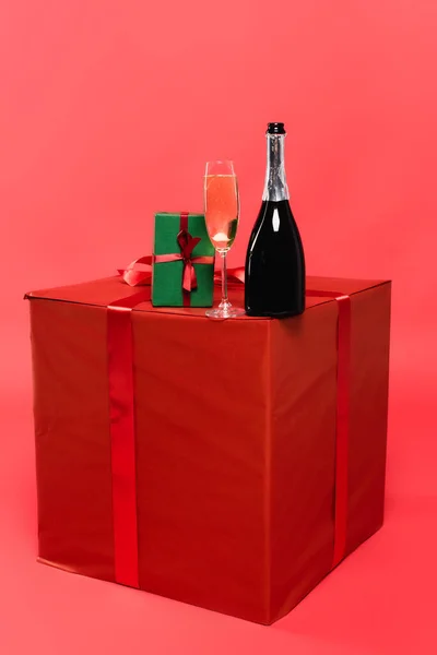 Botella y copa de champán en cajas de regalo sobre fondo rojo - foto de stock