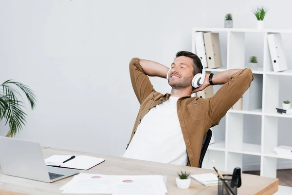 Homme d'affaires souriant avec les yeux fermés se détendre tout en étant assis sur le lieu de travail avec ordinateur portable — Photo de stock