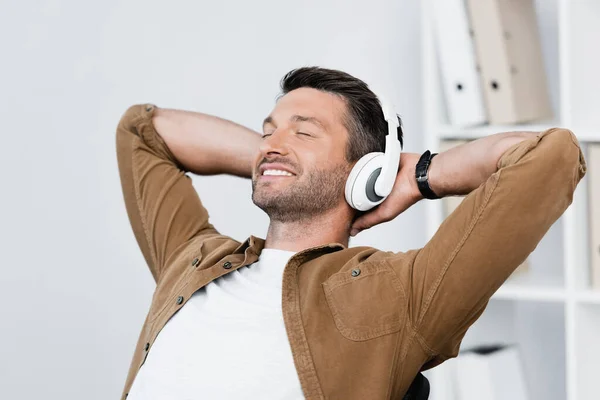 Homme d'affaires souriant dans un casque relaxant tout en écoutant de la musique sur fond flou — Photo de stock