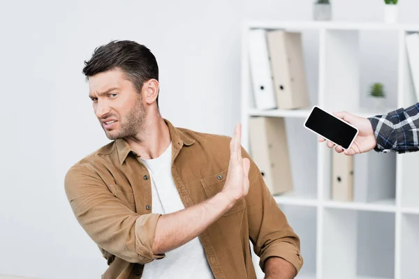 Irritated businessman with stop gesture looking away near smartphone in hand of man — Stock Photo