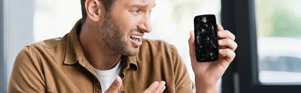 Hombre de negocios asustado mirando el teléfono inteligente aplastado sobre fondo borroso, pancarta - foto de stock