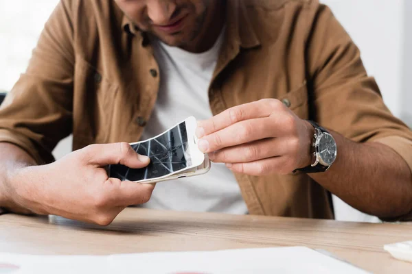 Vista cortada do empresário desmontar smartphone esmagado enquanto sentado à mesa em primeiro plano desfocado — Fotografia de Stock