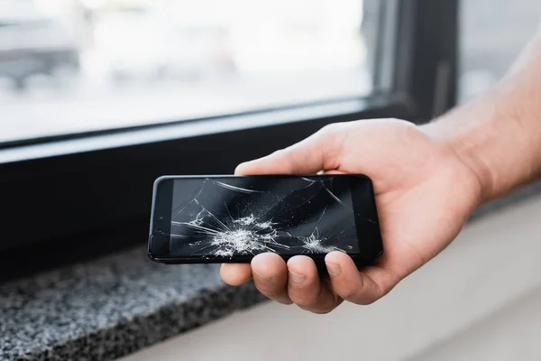 Vista recortada de un hombre de negocios sosteniendo un teléfono inteligente roto sobre un fondo borroso - foto de stock