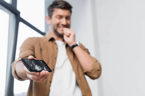 Low angle view of smashed smartphone with blurred scared businessman on background — Stock Photo