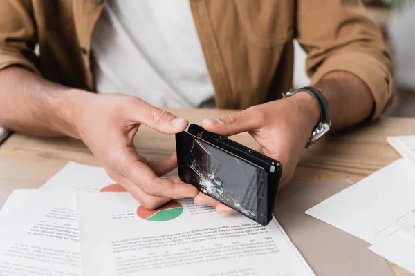 Ausgeschnittene Ansicht von Geschäftsmann zerlegen Smartphone während am Arbeitsplatz mit Papierblättern auf verschwommenem Hintergrund sitzen — Stockfoto