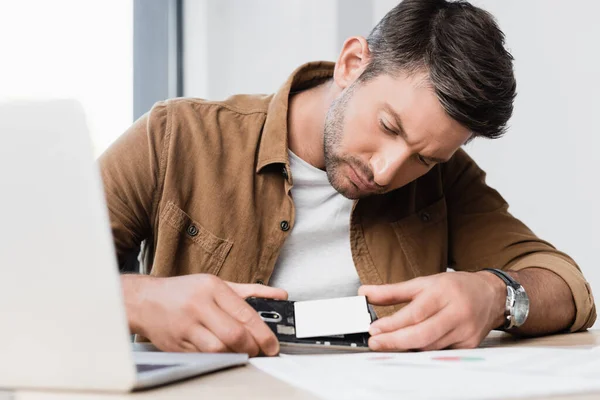 Uomo d'affari concentrato che mette la batteria nel telefono cellulare rotto sul posto di lavoro in primo piano sfocato — Foto stock