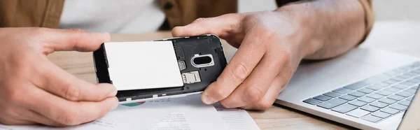 Vista cortada de empresário colocando bateria em telefone celular quebrado na mesa, banner — Fotografia de Stock
