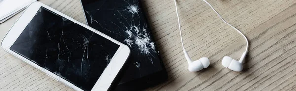 Vue du dessus des écouteurs avec smartphone cassé sur fond en bois, bannière — Photo de stock